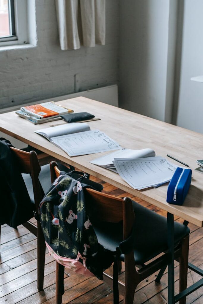 pexels-photo-5905448 Wooden desk with opened copybooks and workbooks placed near chairs with backpacks in light classroom
