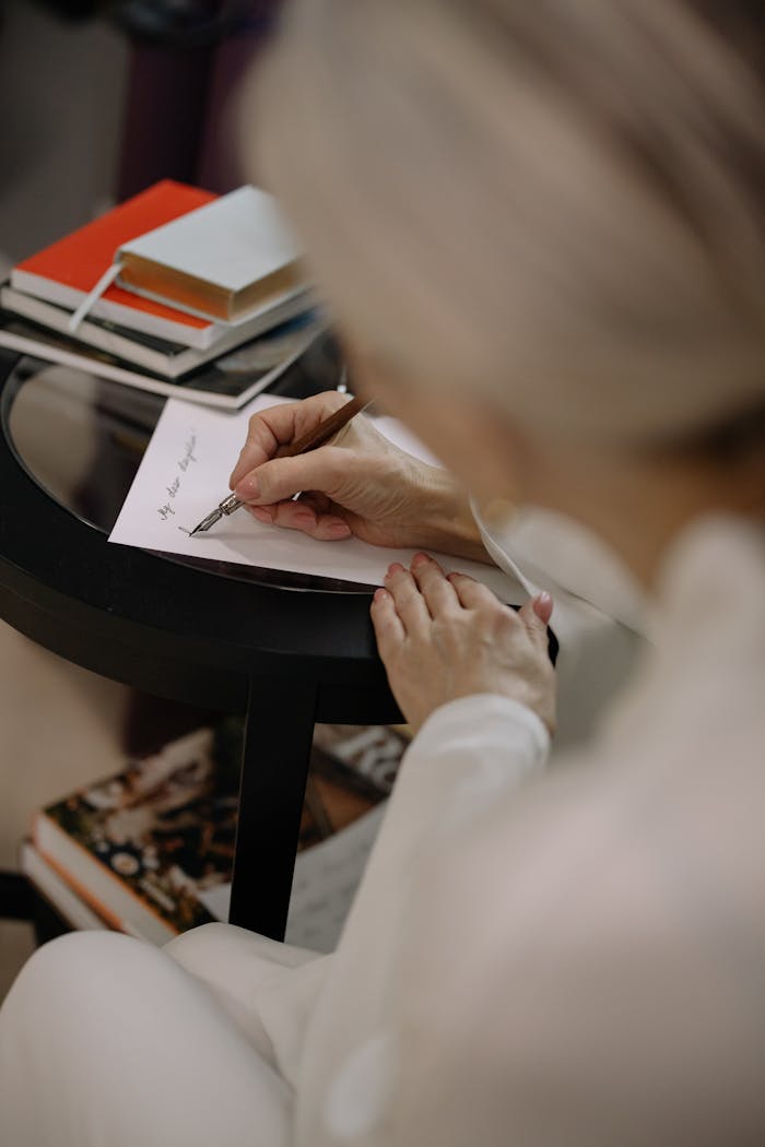 our-story A woman writing a personal note on paper with a pen, next to a stack of books.