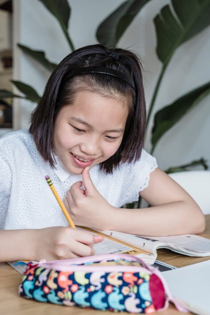 pexels-photo-8055804 Smiling young girl studying at home with her school supplies.